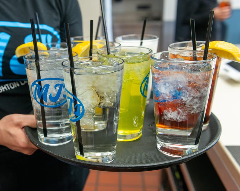 A server carries a tray of various iced drinks with straws and lemon garnishes.